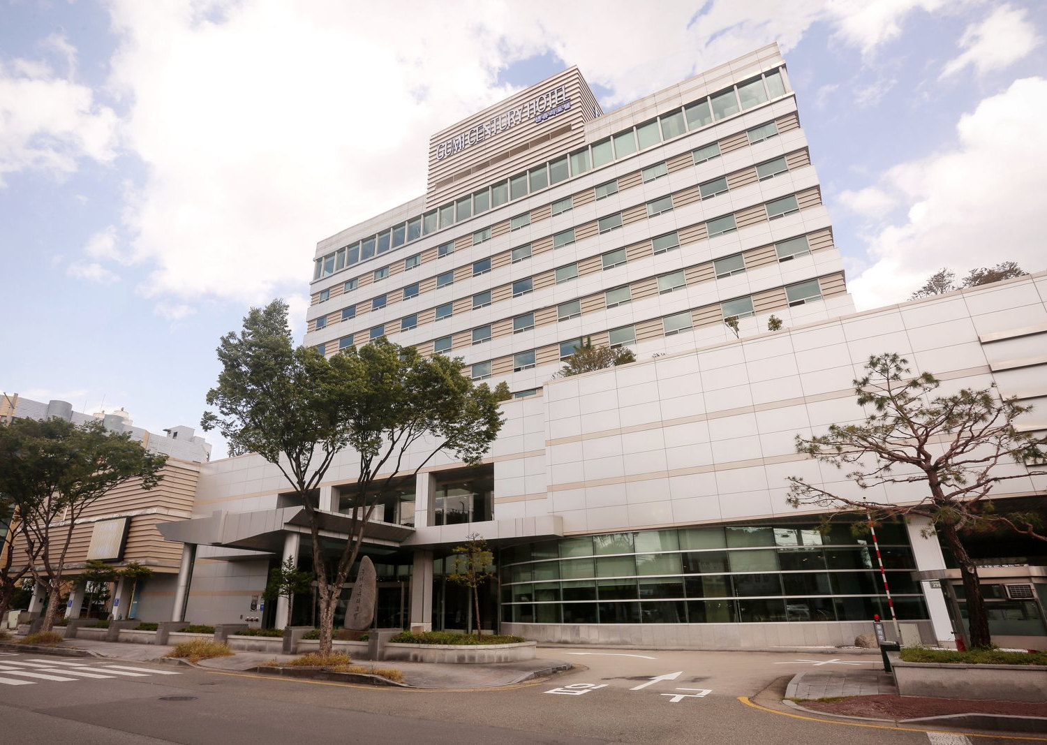 흰 구름 낀 하늘 아래 구미센츄리호텔 정면 — 탑 꼭대기 «GUMI CENTURY HOTEL» 간판과 정문 앞 표지석